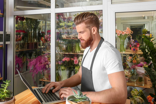 Young handsome florist working with laptop in flower shop