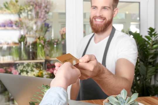 Young handsome florist receiving discount card from regular customer in flower shop