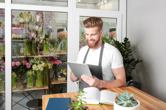 Young handsome florist working with tablet in flower shop