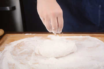 Woman hand adding flour to dough.
