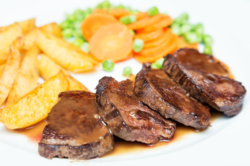 Juicy beef meat steaks with sauce, potatoes, carrots and peas on white plate, close-up. Selective focus