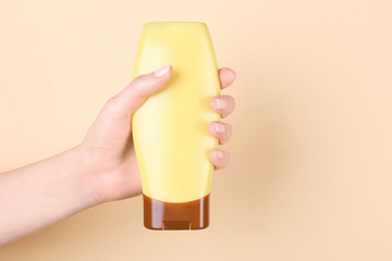 Female hand with bottle of cosmetic product for shower on color background