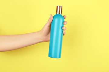 Female hand with bottle of cosmetic product for shower on color background