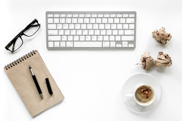 Writer workplace with keyboard, vintage notebook, glasses and coffee on white background top view copyspace
