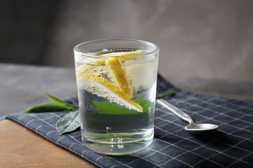 Glass of cold lemon water, spoon and napkin on table, closeup