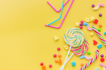 Sweets for birthday including lollipop and drops on yellow background top view copyspace