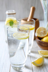 Glasses with cold lemon water on light wooden table, closeup