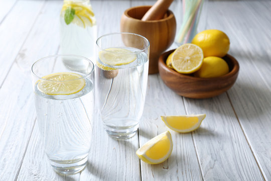 Glasses with cold lemon water on light wooden table