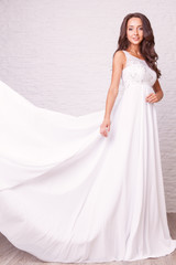 Fototapeta premium Wedding dress. Beautiful curly bride with tan body in white wedding dress pose in studio