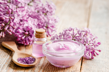 spa cosmetic set with lilac flowers wooden desk background