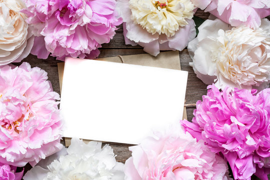 blank greeting card or wedding invitation and envelope in frame of tender peonies flowers