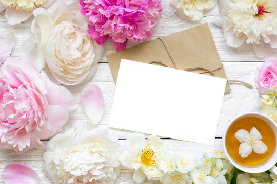 blank greeting card or wedding invitation with tender peonies and roses flowers with cup of green jasmine tea