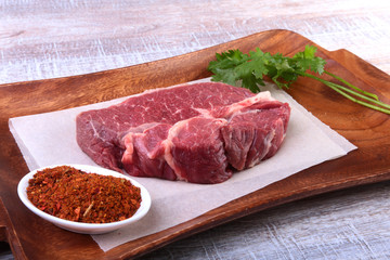 Raw beef steak with spices Leaves of coriander on wooden cutting board. Ready for cooking.