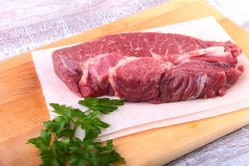 Raw beef steak with spices Leaves of coriander on wooden cutting board. Ready for cooking.