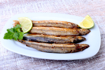 Deep frying small fish capelin and sliced lemon on white plate. Good snack to beer.