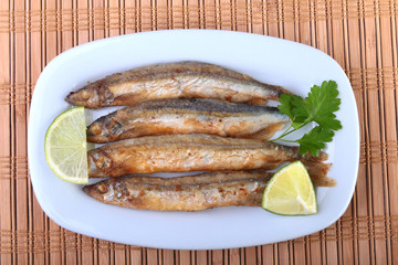 Deep frying small fish capelin and sliced lemon on white plate. Good snack to beer.