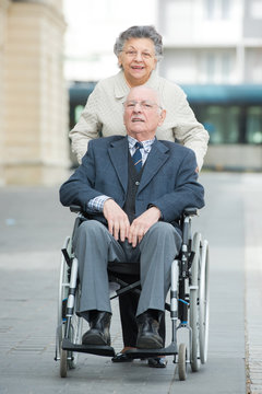 senior lady pushing her husband in his wheelchair