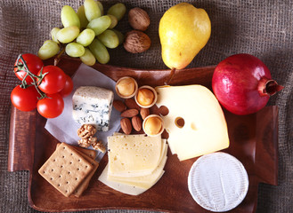 Assortment of cheese with fruits, grapes and nuts on a wooden serving tray.