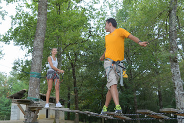 couple with safety equipment on wooden bridge between trees