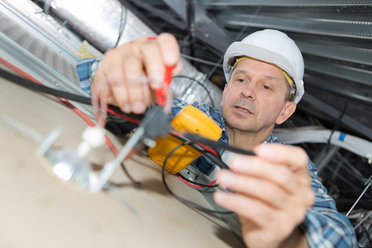 electrician repairing wiring inside office ceiling