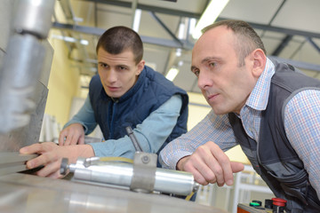 engineer showing apprentice how to use tool in factory