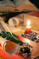 Quill pen, old papers and books by candle light