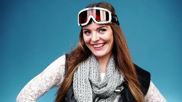 Woman smiling skier girl wearing warm clothing ski goggles portrait. Winter sport activity. Beautiful long hair sportswoman on blue studio shot, full HD.