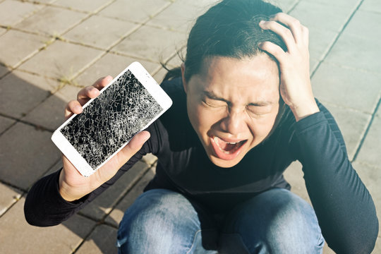 Screaming woman  holding a screen crack the smartphone outdoor.