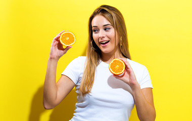 Happy young woman holding oranges halves on a yellow background