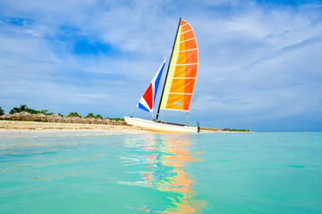 The tropical beach of Varadero in Cuba with a colorful sailboat