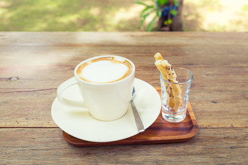 Coffee cup and pastry on wooden table with nature background.