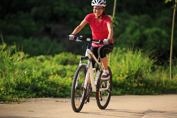 woman cyclist cycling on summer forest trail
