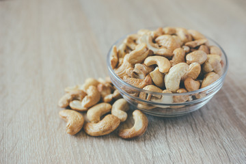 Glass bowl with cashew nuts on wooden background