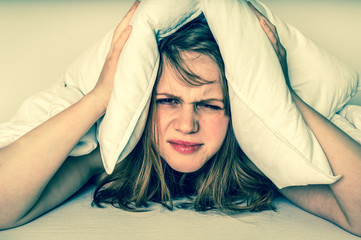 Woman in bed covering ears with pillow because of noise