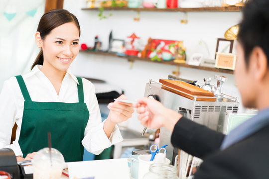 Barista is making coffee at his restaurant. and own a coffee shop she is swiping credit card. Where customers are paying