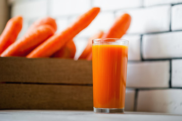 Refreshing smoothies of carrots, pumpkins, mangoes and a box of carrots against a white wall. Glass with carrot smoothies and carrots