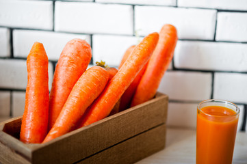 Refreshing smoothies of carrots, pumpkins, mangoes and a box of carrots against a white wall. Glass with carrot smoothies and carrots