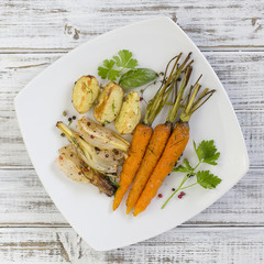 Young potatoes, carrots, onions, peppers, garlic baked in the oven on the white plate. Top view