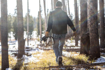 Man walking through forest with chainsaw in winter