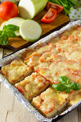 Baked zucchini with meat, rice, tomatoes and cheese on a wooden kitchen table.