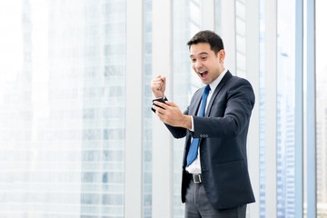 Businessman yelling and raising his fist with delighted feeling while looking at mobile phone