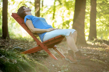 erwachsene Frau sitzt auf rotem Stuhl im Wald und entspannt und erholt sich