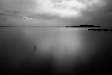 Mininalist view of a lake, with a wooden pole in the foreground and a pier in the background