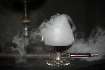 Heavy hookah smoke with a brandy glass on a gray background, hookah tube
