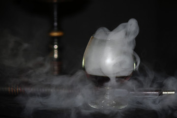 Heavy hookah smoke with a brandy glass on a gray background, hookah tube