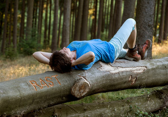 Frau liegt entspannt auf Baumstamm in den das Wort Rast eingeritzt ist