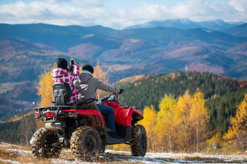 Man manages quadbike, girlfriend sitting behind him makes photo of beautiful landscape mountains and forest on the phone © anatoliy_gleb