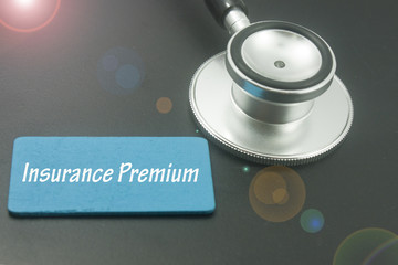 stethoscope with wooden tag written insurance premium isolated on black background