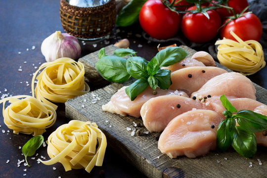 Fresh meat. Preparation of Italian cuisine pasta with chicken fillet, various spices and tomatoes on dark concrete, stone or slate. Food background.