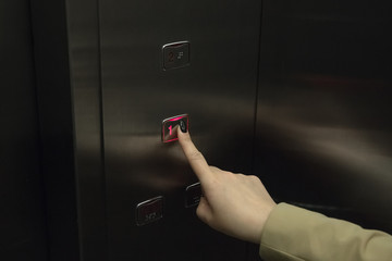 Female finger presses the button on the elevator to go to the first floor
